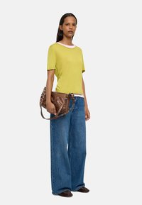 Lime zielona koszulka z krótkim rękawem z różowym dekoltem, w zestawieniu z szerokimi niebieskimi dżinsami. Brązowa skórzana torba z paskiem i metalowymi akcentami.