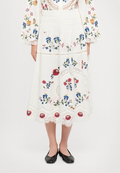 White embroidered skirt featuring colorful floral patterns, scalloped lace hem, and a fitted waist. Paired with black flat shoes.