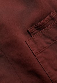 Burgundi kangas tekstureeritud pinnaga, külgpocket, millel on pealmine õmblusdetail. Materjal näeb välja vastupidav ja struktureeritud.