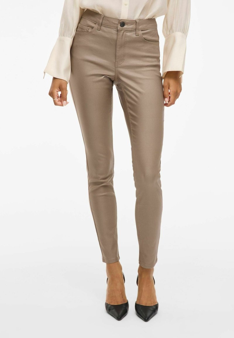 Pantalon skinny en tissu lisse marron clair avec une taille haute et des poches avant, associé à des chaussures à talons noires.