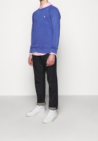 Suéter azul de cuello redondo sobre una camisa de color rosa con cuello, acompañado de jeans oscuros y zapatillas blancas. Logotipo notable en el suéter.