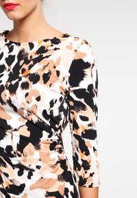 Sukienka w zwierzęcy wzór z mieszanką czerni, beżu i bieli. Tkanina jest gładka, sukienka ma dopasowany krój i rękawy o długości trzech kwart.