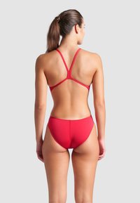 Bikini rouge avec un design sportif, des bretelles croisées réglables et une coupe minimaliste au bas. Texture lisse et tissu extensible.