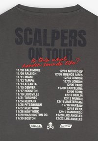 Camiseta de algodón gris con texto grande en la parte posterior que dice "SCALPERS ON TOUR", fechas, nombres de ciudades y un logo de calavera en la parte inferior.