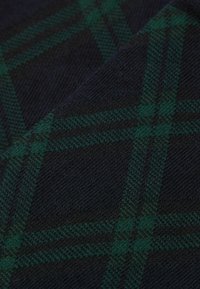 Wełniana tkanina w ciemnym granacie z zielonym kratkowanym wzorem tartan. Tekstura jest miękka i dziana, z ukośnymi liniami i przecinającymi się paskami.