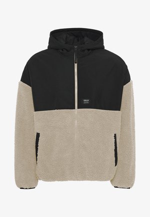 Hættetrøje med en sort øverste del og en cremegul fleece nederste del, med lynlås lukning og sidelommer; blød tekstur.