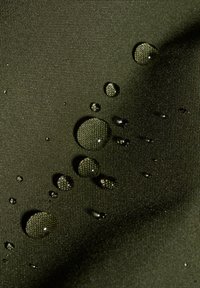 Tessuto verde resistente all'acqua con una superficie testurizzata, caratterizzato da molteplici gocce d'acqua di diverse dimensioni, che evidenziano le sue proprietà idrofobiche.