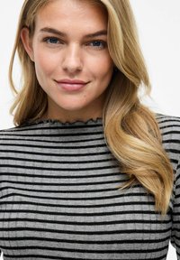 Grå och svart randig topp med ribbad textur och vågig halsringning. Långt hår delvis synligt på ena sidan.