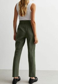 Pantaloni su misura verde oliva con design a gamba dritta, vita media e una sola tasca sul retro, abbinati a scarpe nere.