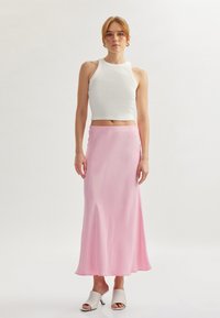Un crop top blanc côtelé associé à une longue jupe maxi en satin rose fluide et des mules à talons ouverts blanches. Des textures lisses et une silhouette élégante.
