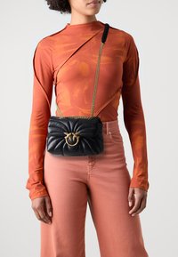 Zwart leren crossbody tas met een gequilt textuur, gouden hardware en een onderscheidende sluiting. De kettingband voegt een vleugje elegantie toe.