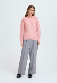 Ljusrosa stickad tröja med texturmönster, kombinerad med ljusgrå vida byxor, bärs med svarta slip-on-skor.