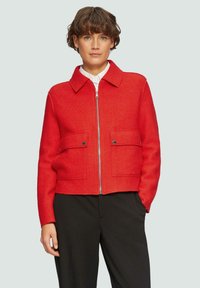 Czerwona krótka kurtka z kołnierzykiem, dwoma przednimi kieszeniami i metalowym zamkiem błyskawicznym. Wykonana z teksturowanej tkaniny, z kontrastowym niebieskim detalem zamka.