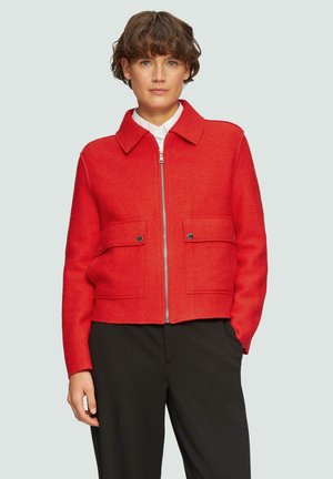 Rode cropped jas met een kraag, twee voorzakken en een metalen rits. Gemaakt van een textuurstof, met contrasterende blauwe ritsdetails.