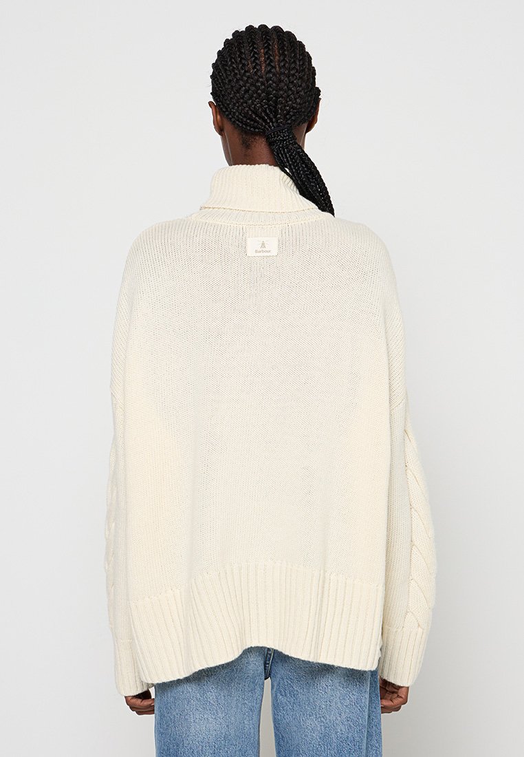 Cremfarbener Strickpullover mit hohem Kragen, Zopfstrickdetail an den Ärmeln und geripptem Saum, sowie einem dezenten Logosticker auf der Rückseite.