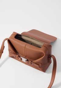 Brown leather handbag with a structured shape, open top, contrasting interior, and a front buckle detail. The strap is adjustable.