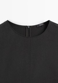 Schwarzes Kleid mit runder Ausschnitt, Reißverschluss hinten und subtiler Textur. Etikett liest "Massimo Dutti." Taillierte, strukturierte Form ohne Muster.