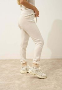 Beige joggerit, joissa on pehmeä tekstuuri, ribatut hihnat ja naru vyötäröllä, yhdistettynä vaaleanvärisiin lenkkitossuihin, joissa on verkkosalamet.