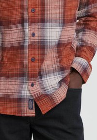 Ruitjes overhemd in rood en wit flanel met marineblauwe accenten, beschikt over knoopsluiting en lange mouwen. Gestructureerde stof met zichtbare stiksels.