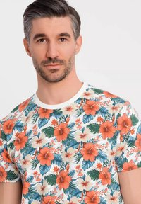 Het T-shirt met korte mouwen heeft een witte basis met een levendig bloemenpatroon, waaronder oranje hibiscusbloemen en groene bladeren.