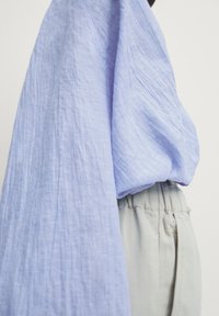 Haut en lin bleu clair avec une finition texturée, doté de manches surdimensionnées. Associé à un bas gris clair avec une taille élastique, soulignant une coupe décontractée.