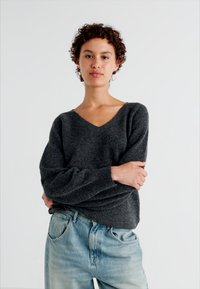 Maglione grigio a collo a V con maniche lunghe e larghe, realizzato in materiale morbido. Abbinato a jeans di denim azzurri, che mostrano una vestibilità rilassata.