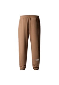 Bruine trainingsbroek met een zachte textuur, een elastische tailleband en een boord aan de enkels. Heeft een wit logo op de linkeronderbeen.