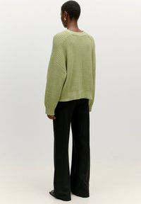 Gestrickter, übergroßer grüner Pullover mit geripptem Textur, weiten Ärmeln und einem cropped Saum, kombiniert mit schwarzen, weit geschnittenen Hosen.