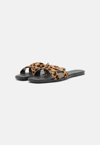 Leopard print sandals with two crossed straps, black flat sole, and smooth texture. Ideal for casual wear.