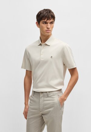 Lichtbeige polo shirt met korte mouwen en een kraag, drie knopen en een klein logo op de borst, gecombineerd met lichtgrijze broek.