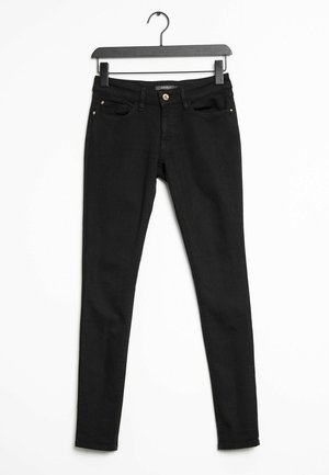 Jeans skinny noirs avec une texture denim lisse. Comprend cinq poches et une fermeture à bouton en métal. Suspendus à un cintre en plastique noir.