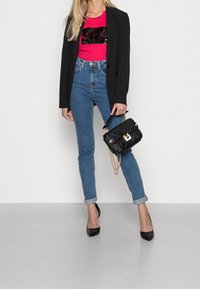 Blazer negro, top de lentejuelas rosa, jeans azules de cintura alta y tacones negros de punta. Llevando un bolso negro acolchado con detalles dorados.
