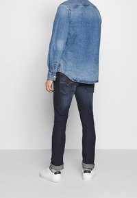 Denim-paitasi pitkähihaisena ja kaarrettuna helmana, vaaleansininen väri. Parit tummansiniset farkut ja valkoiset lenkkarit mustilla yksityiskohdilla.