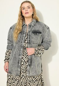 Šedá denimová košile s knoflíkovým zapín�áním vpředu, dvěma kapsami na hrudi a spadlými rameny. Nosená přes šaty s černobílým zebra vzorem.