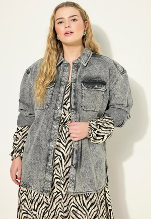 Šedá denimová košile s knoflíkovým zapínáním vpředu, dvěma kapsami na hrudi a spadlými rameny. Nosená přes šaty s černobílým zebra vzorem.