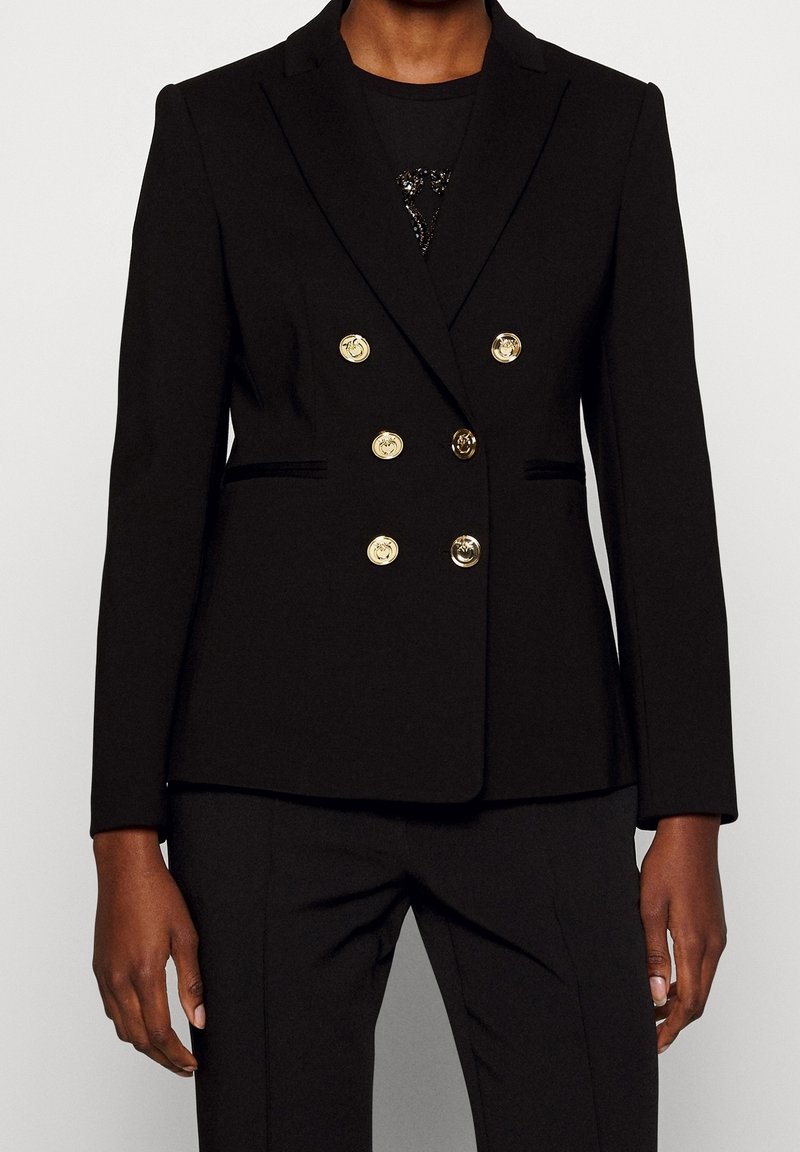 Blazer doppiopetto nero su misura con sei bottoni dorati indossato sopra pantaloni neri, mostrato dalle spalle a metà coscia su sfondo uniforme.