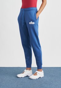 Modré tepláky s elastickým pásom a �šnúrkou, s bielym logom Nike. Elastické lemy na nohaviciach a vrecká po bokoch.