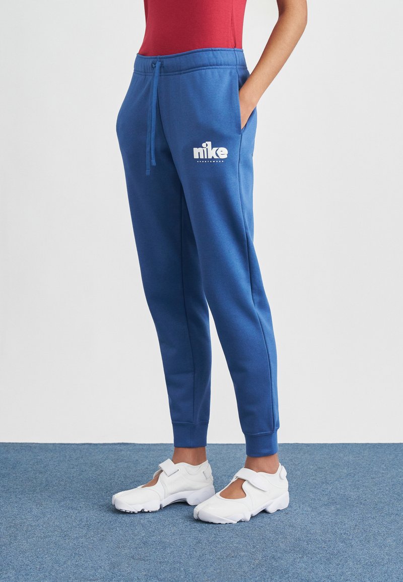 Modré tepláky s elastickým pásom a šnúrkou, s bielym logom Nike. Elastické lemy na nohaviciach a vrecká po bokoch.