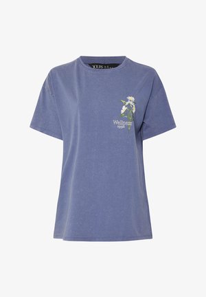 Lavendelblauw T-shirt met korte mouwen, kleine witte madeliefjesgrafiek en de tekst "Wellness 1998" aan de linkerkant van de borst.