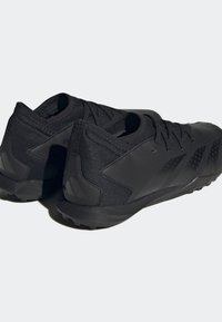 Svarta atletiska skor med en texturerad mesh-övre, rund tå, plana snören och ett mönstrat gummisula med lätta mönster för grepp.