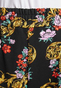 Czarny materiał z kwiatowym wzorem w kolorach czerwonym, różowym i niebieskim, z złotymi ozdobnymi akcentami. Elastyczny pas z teksturowaną powierzchnią.