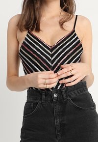 Top sans manches noir avec des rayures en chevron multicolores en sequins blancs, roses et argentés. Associé à un short en denim noir taille haute.