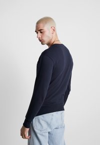 Sudadera de cuello redondo azul marino con mangas largas, puños y dobladillo acanalados. Tejido suave con una textura lisa, ajustada en la cintura.