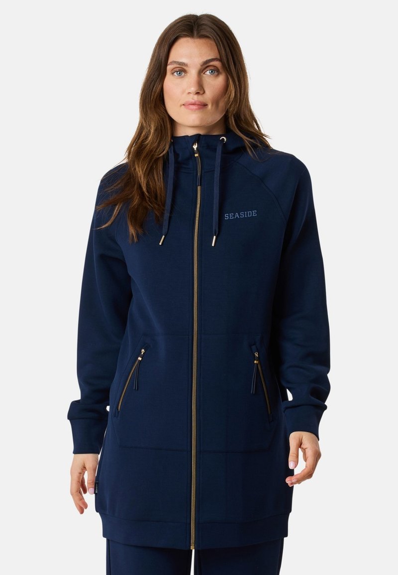 Felpa zip con cappuccio di colore blu navy, dotata di hardware dorato, cappuccio regolabile e due tasche frontali. Realizzata in tessuto morbido con una texture liscia.
