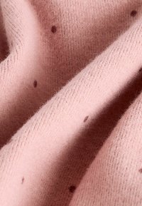 Rosa stickat tyg med en mjuk textur, prydd med små bruna prickar som är spridda över ytan och skapar ett subtilt mönster.