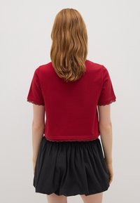 Camiseta corta roja con mangas cortas y adornos de encaje en los puños y el dobladillo, combinada con una falda negra que tiene una textura fruncida.