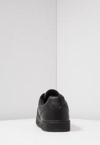 Baskets en cuir noir avec semelle noire estampillée, vues de dos sur une surface blanche avec un fond blanc uni.