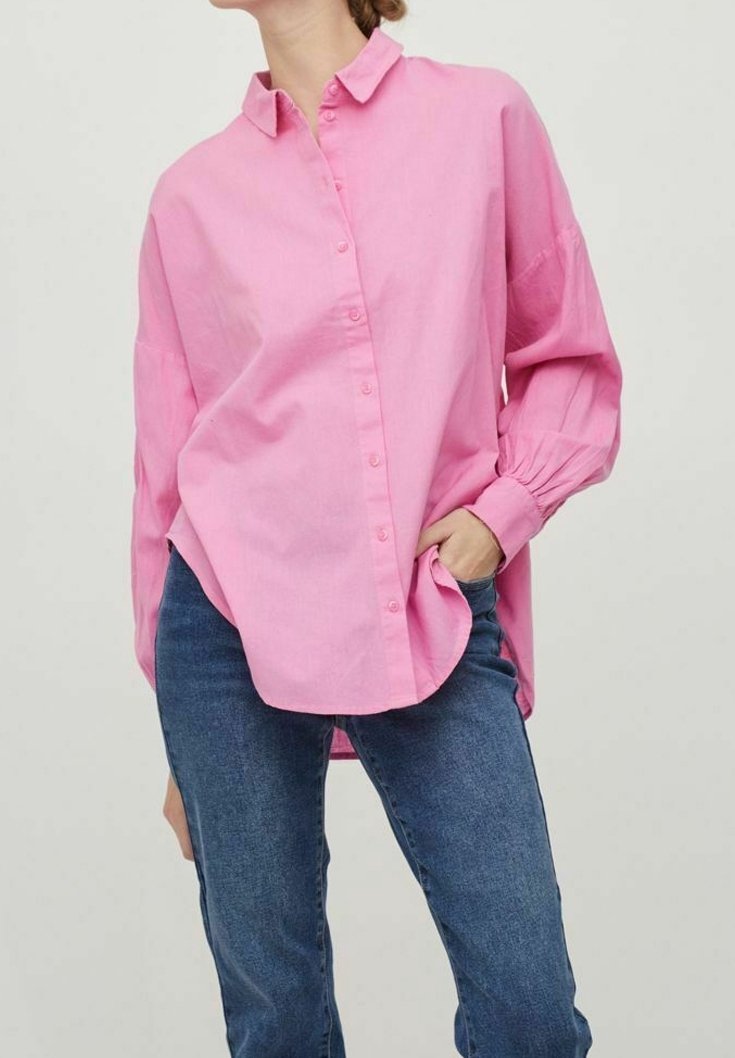 Helles rosa Hemd mit Kragen, langen Ärmeln und Raffung an den Manschetten, kombiniert mit blauen Jeans.