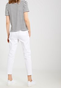 Pruhované bavlněné tričko v béžové a černé barvě, kombinované s bílými slim-fit kalhotami a bílými teniskami. Oblečení má ležérní design.