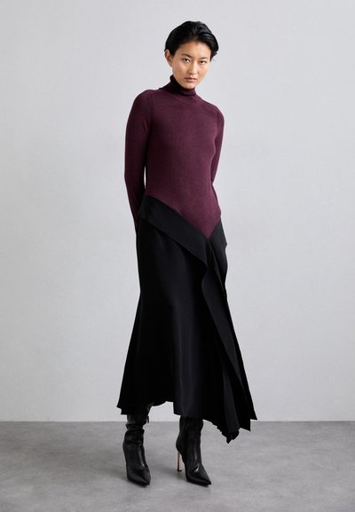 Burgundijas turtlenecks džemperis kombinēts ar melnu asimetrisku svārku. Tērps izceļas ar elegantiem tekstūrām un asām līnijām. Melni norādīti zābaki papildina izskatu.